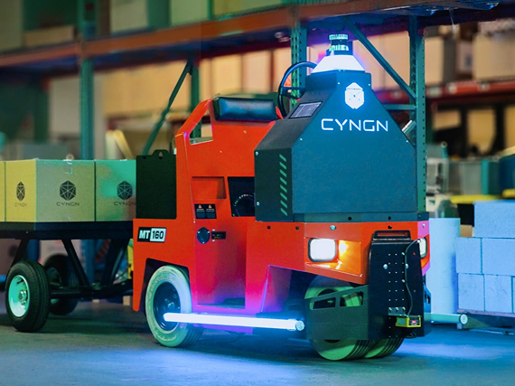 Cyngn DriveMod Tugger autonomous vehicle towing a loaded cart in a warehouse